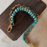 Turquoise beaded bag charm with gold chain on a wooden block, J Forks & Leather and Vodka