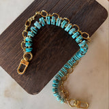 Turquoise beaded bag charm with gold chain on a wooden block, J Forks & Leather and Vodka