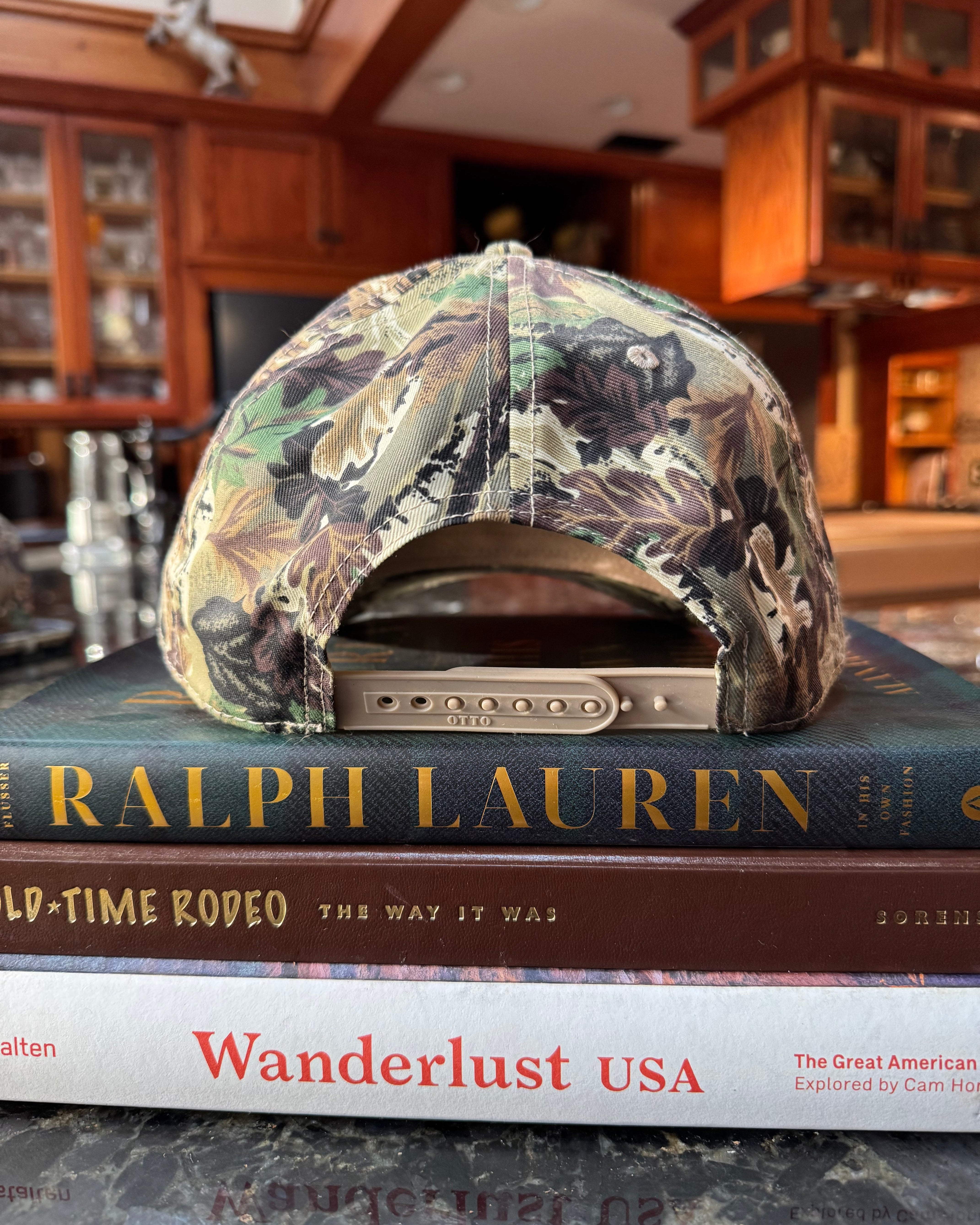 Camouflage-patterned hat on top of a book titled 'Wanderlust USA' with a blurred indoor background.