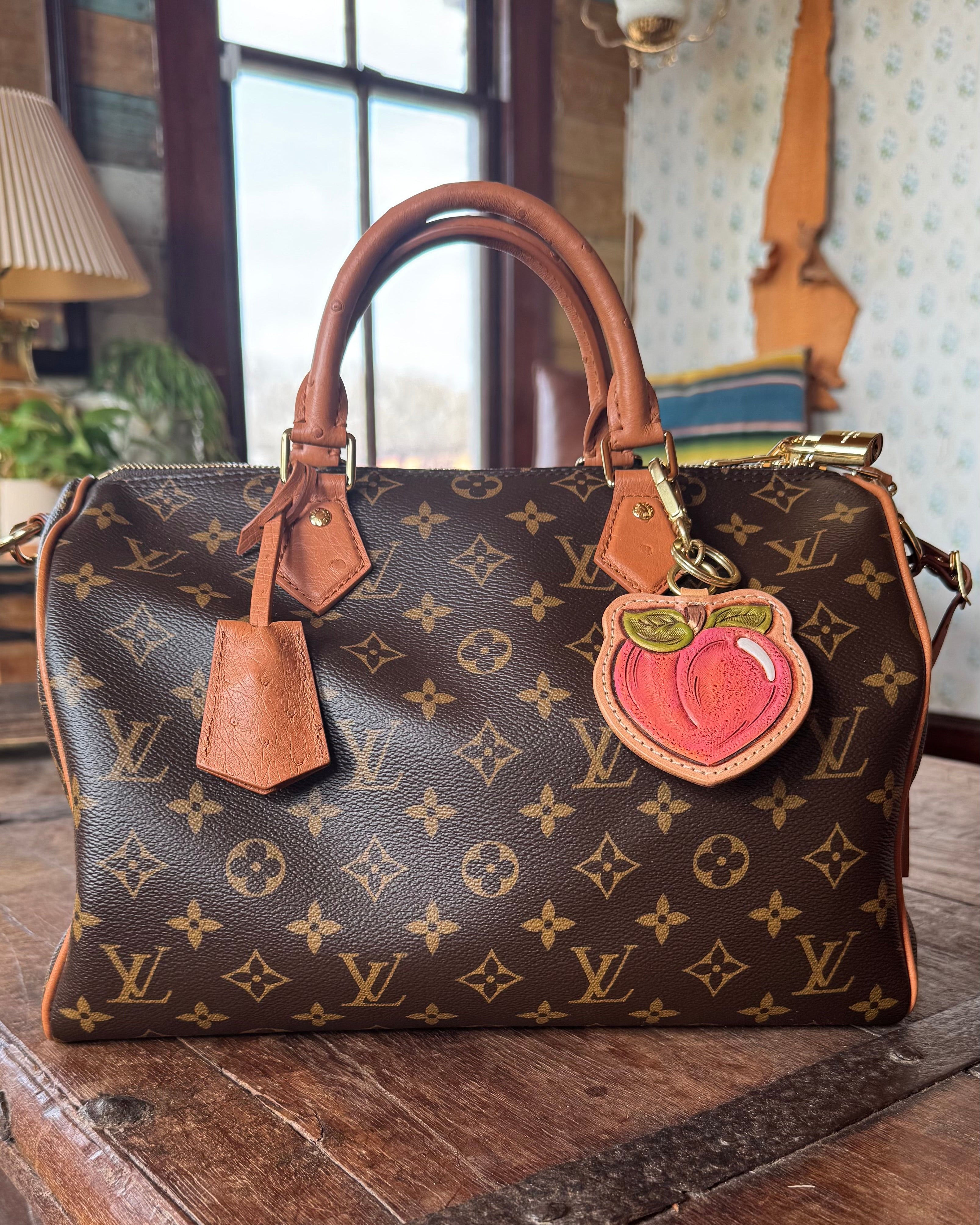 Luxury handbag with monogram pattern, revamped by Leather and Vodka with leather peach bag charm, sitting on wooden table