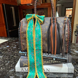 Designer handbag with a green and yellow patterned twilly on a marble surface.
