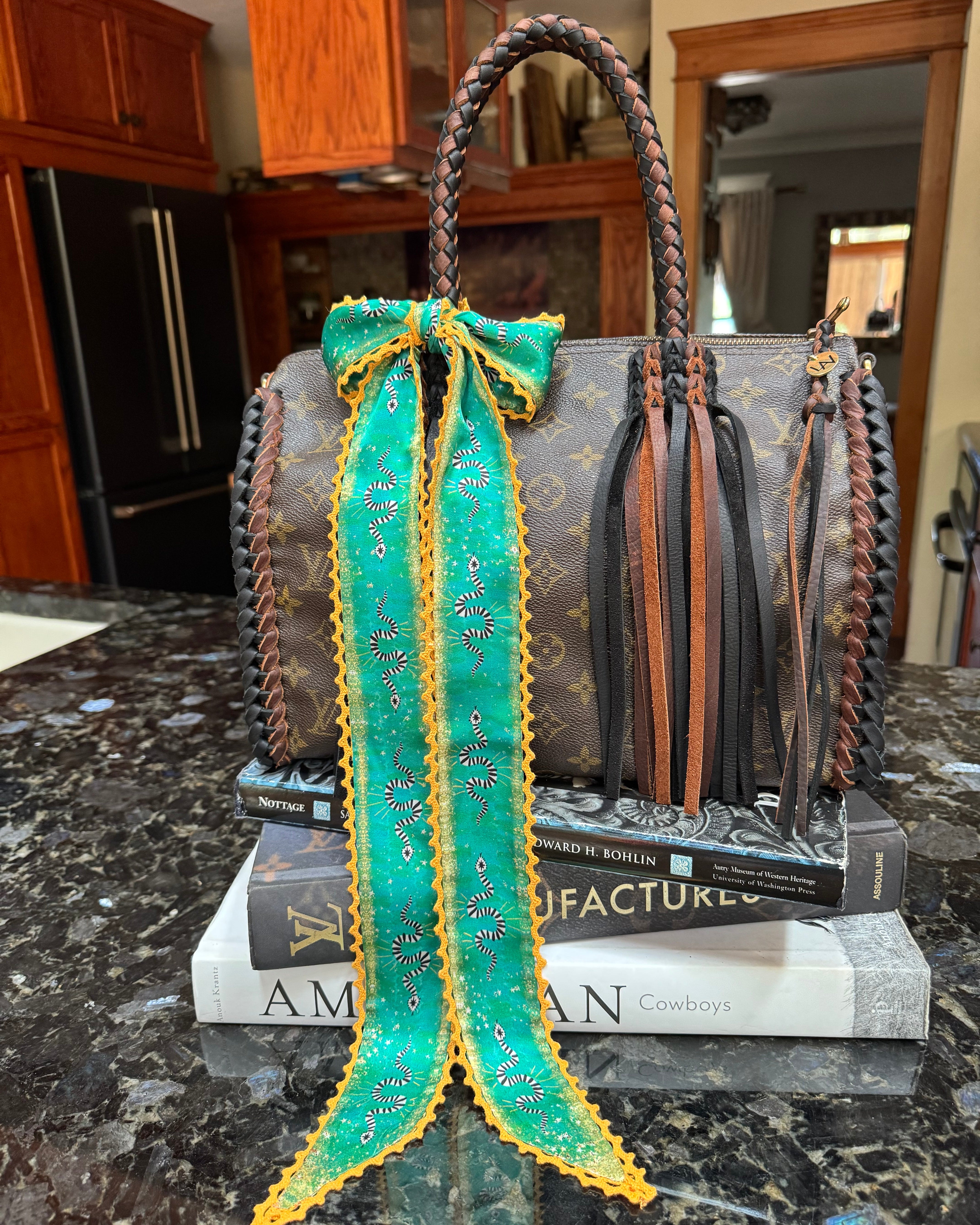 Designer handbag with a green and yellow patterned twilly on a marble surface.