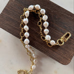 Gold hand bag chain with pearl-like beads on a wooden block