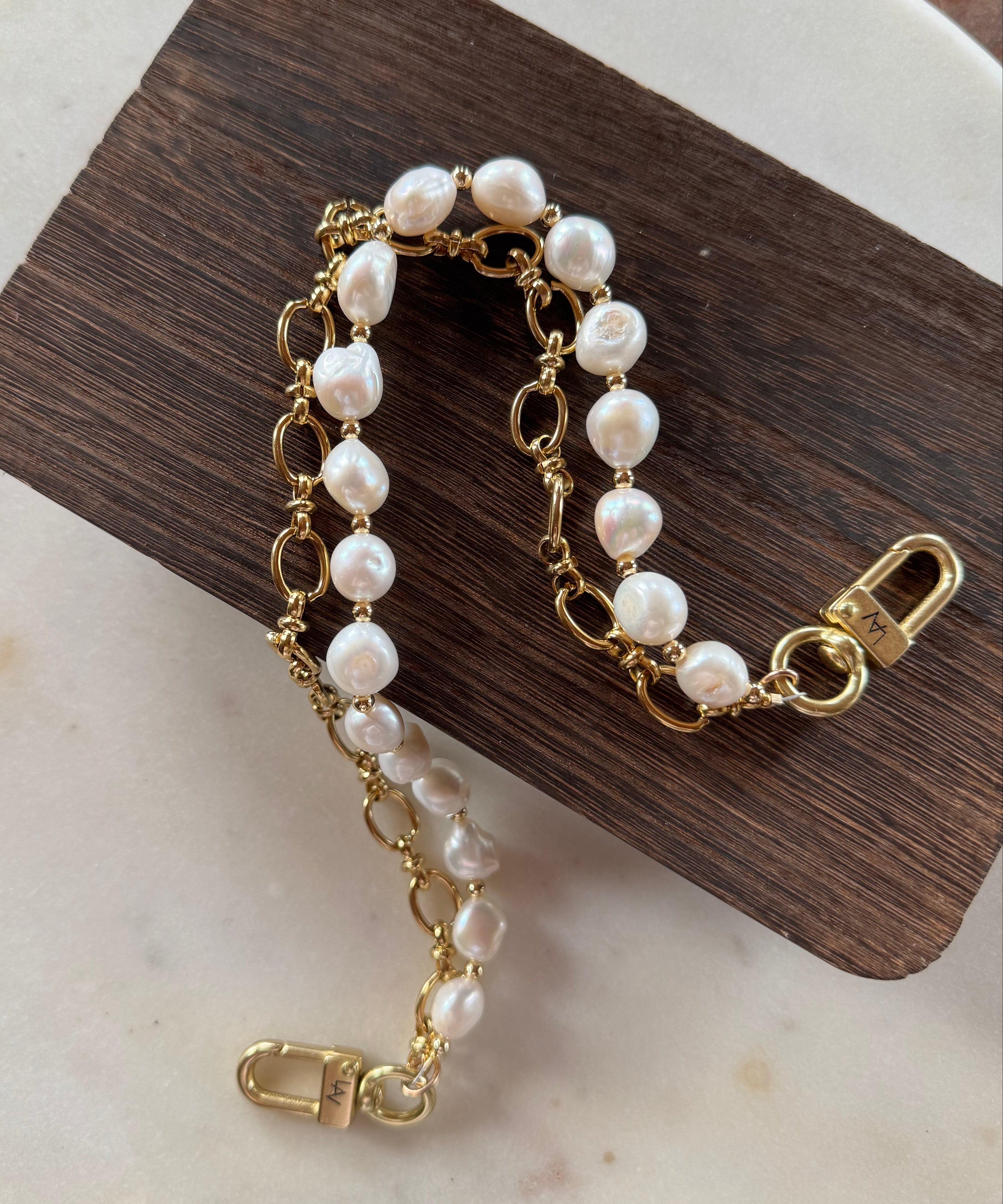Gold hand bag chain with pearl-like beads on a wooden block