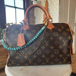 Designer handbag with monogram pattern on a surface adorned with Turquoise beaded bag chain with gold chain on a wooden block, J Forks & Leather and Vodka