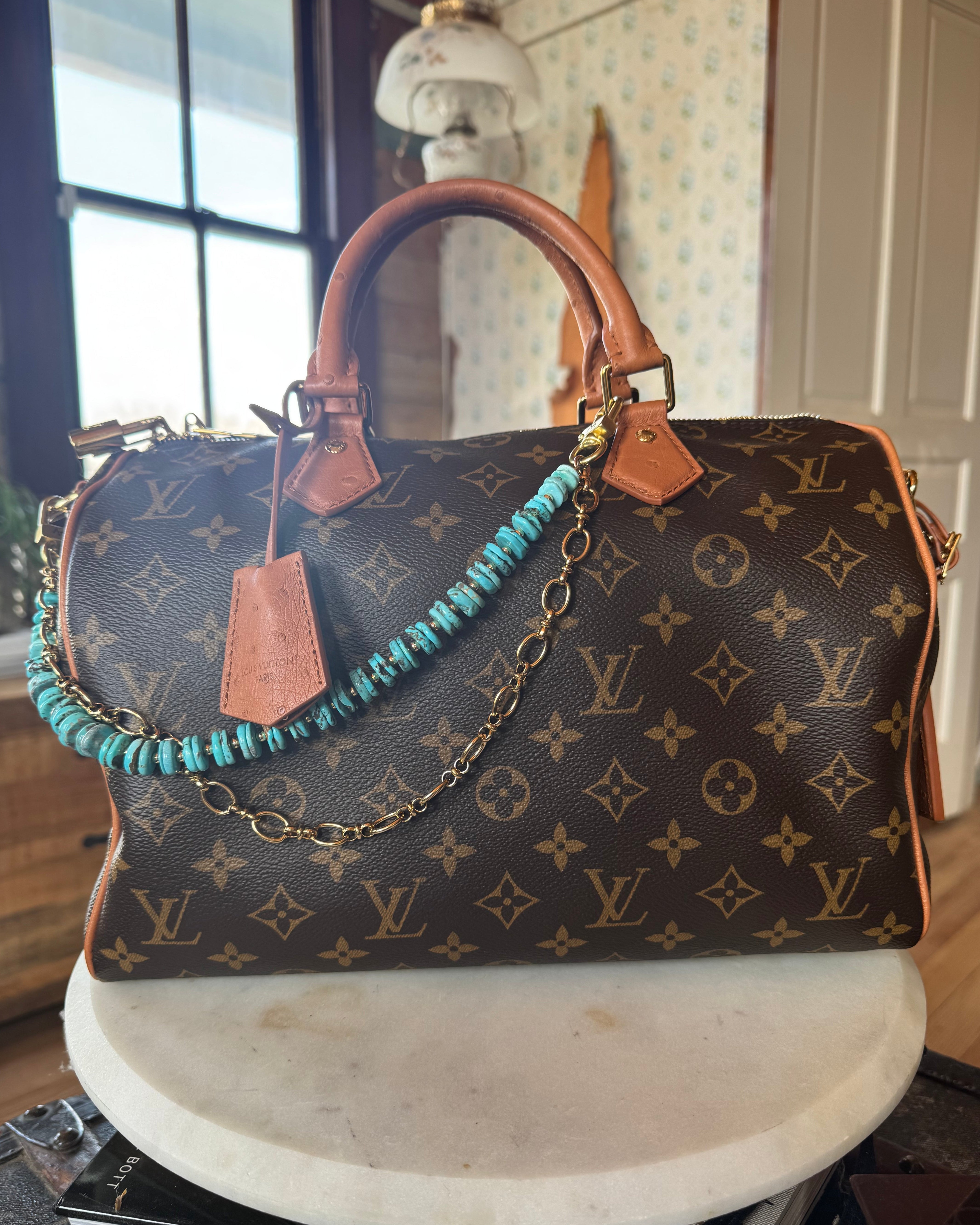 Designer handbag with monogram pattern on a surface adorned with Turquoise beaded bag chain with gold chain on a wooden block, J Forks & Leather and Vodka