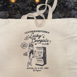 A beige cotton tote bag with a printed logo featuring an illustration of a cowgirl and a slot machine, text mentioning 'Leatherandvodka', 'Lucky Cowgirls Club', and 'Austin, TX'. The bag also includes the text 'NFR 2024' and has a graphic indicating a five-day event.