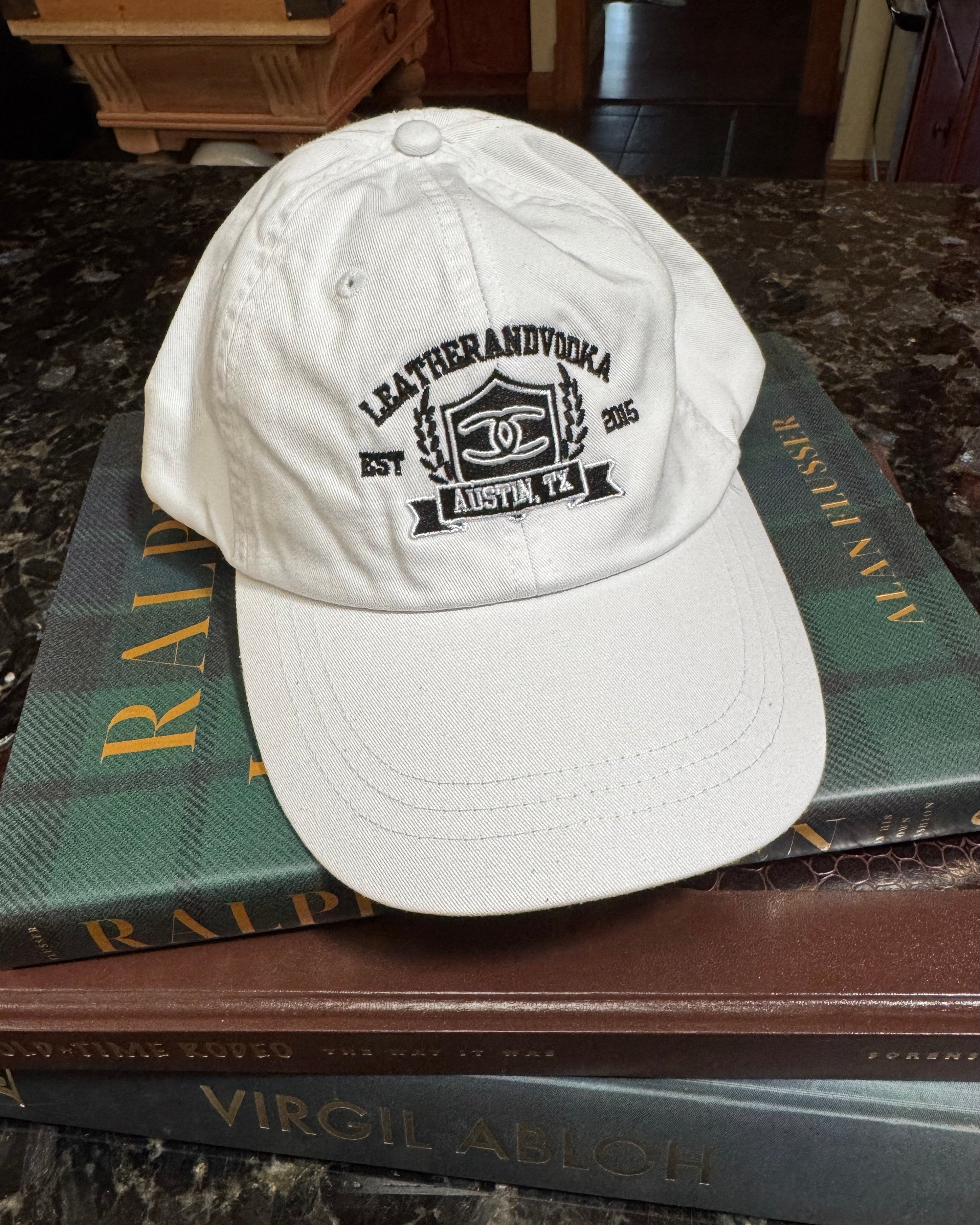 Whitebaseball cap with leatherandvodka embroidery sitting on books on marble counter top