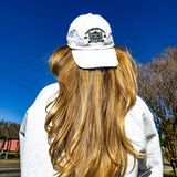Person wearing a white cap and sweater with long blonde hair, standing outdoors on a clear day.
