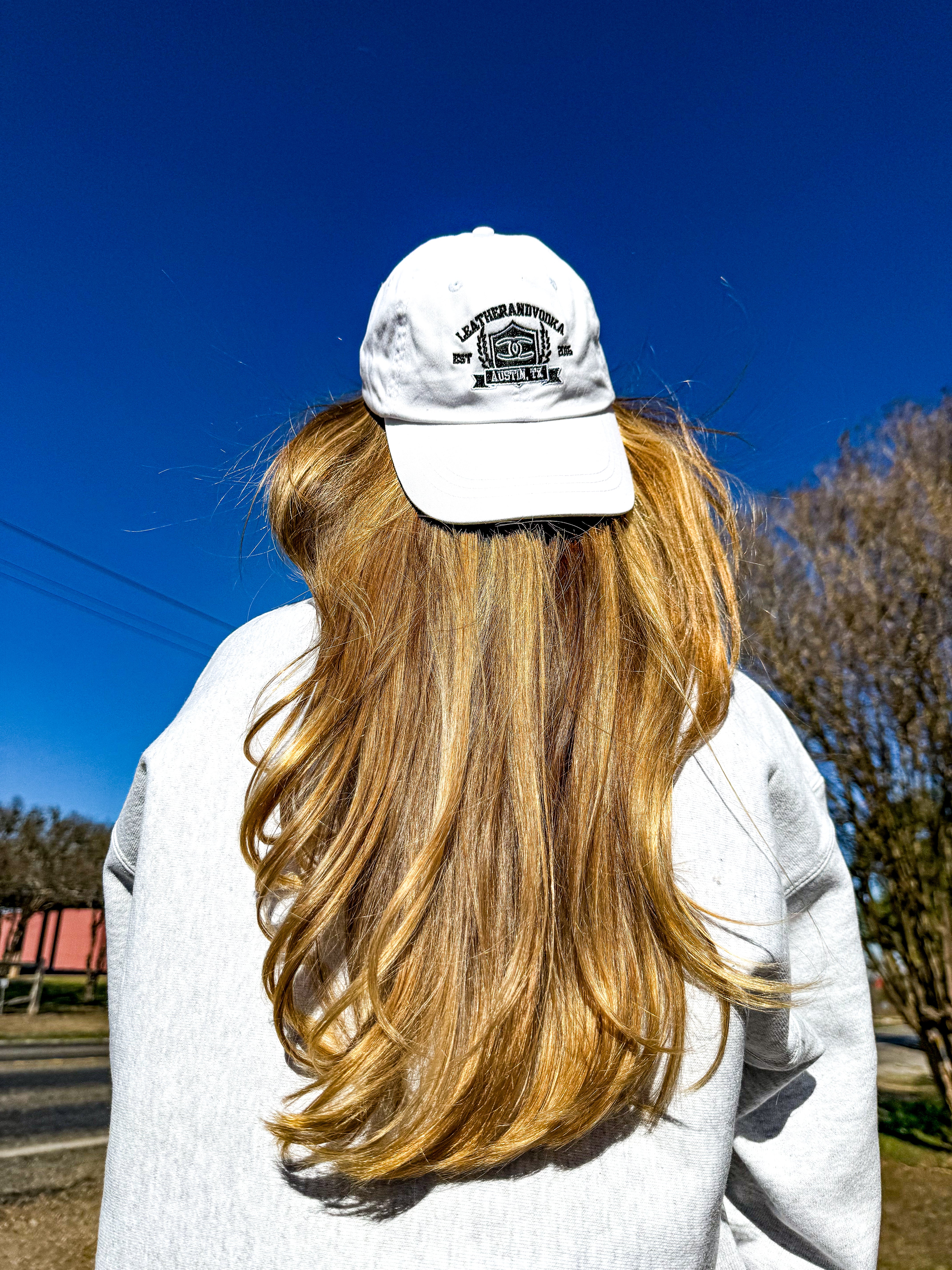 Person wearing a white cap and sweater with long blonde hair, standing outdoors on a clear day.