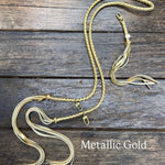 Metallic Gold Bag Strap, made with braided leather with matching snap on key chain, laying on wooden table. 