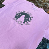 Pink t-shirt with a green graphic design on a textured surface