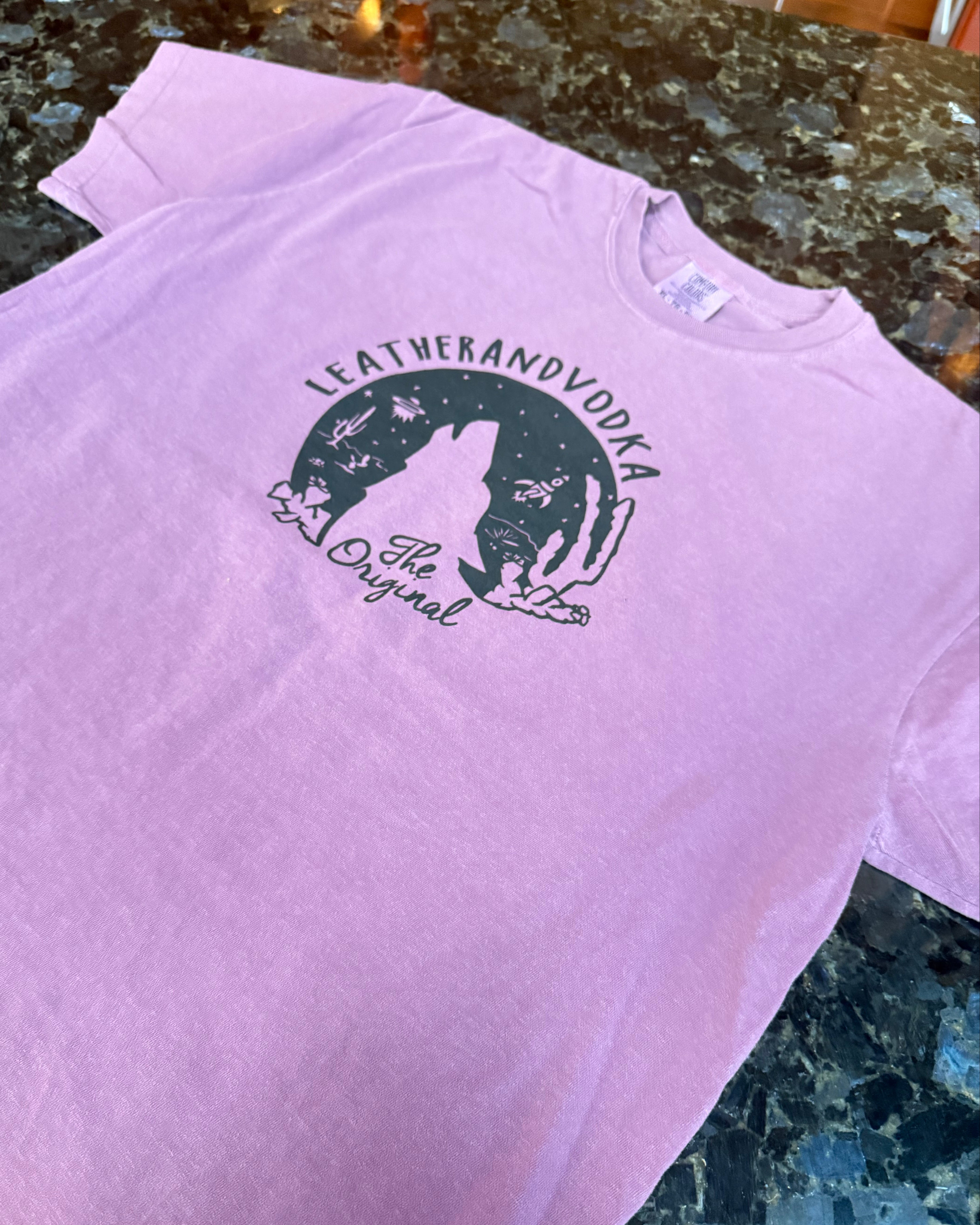 Pink t-shirt with a green graphic design on a textured surface