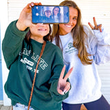 Two people taking a selfie with a phone, one wearing a green LAV branded sweatshirt and the other in a LAV branded white sweatshirt.