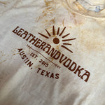 Leather and Vodka logo on a tye-dye t-shirt, laying flat on table.