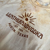 Leather and Vodka logo on a tye-dye t-shirt, laying flat on table.