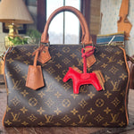 Designer handbag with a Hermes red horse bag charm on a wooden surface