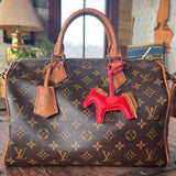 Designer handbag with a Hermes red horse bag charm on a wooden surface