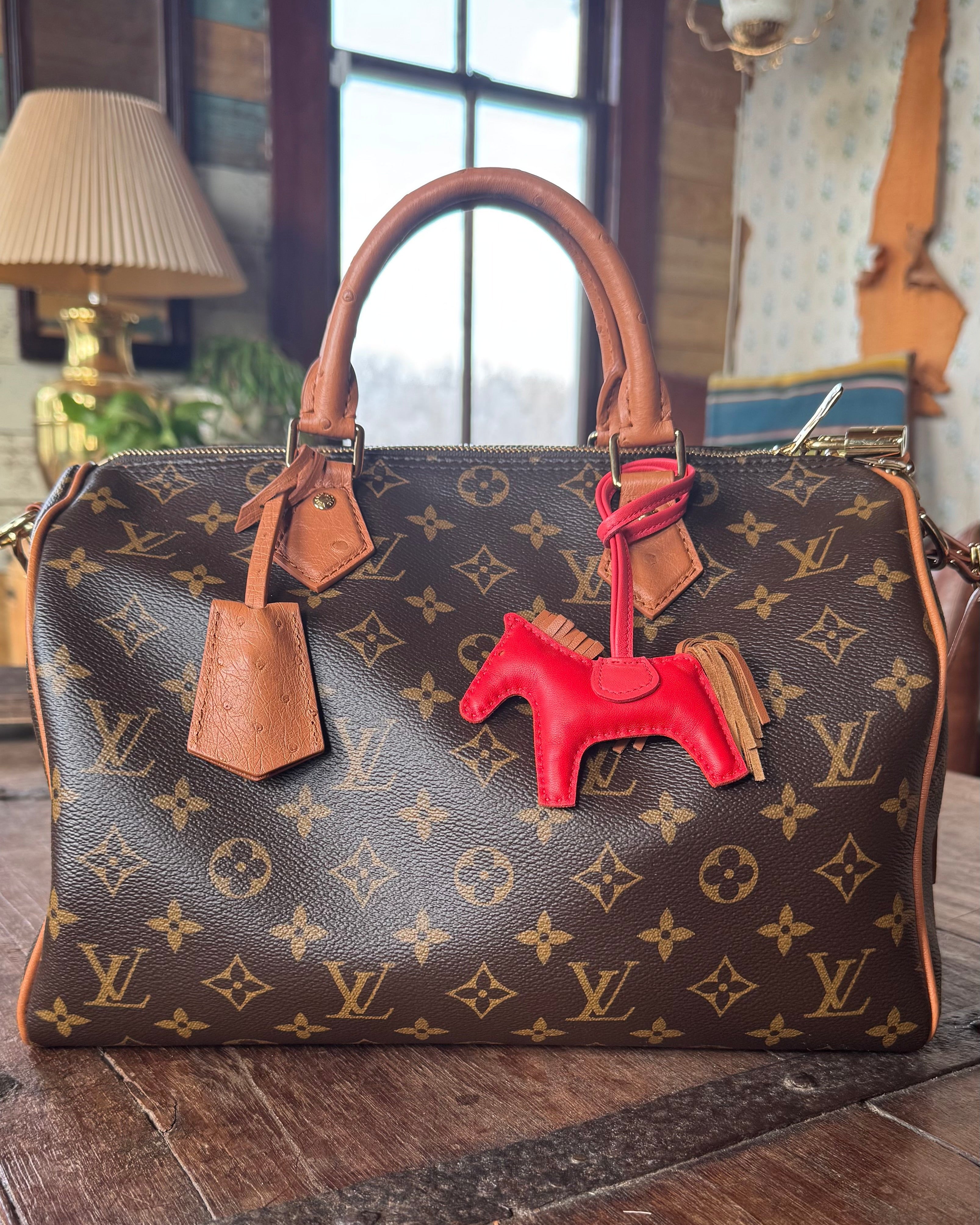 Designer handbag with a Hermes red horse bag charm on a wooden surface