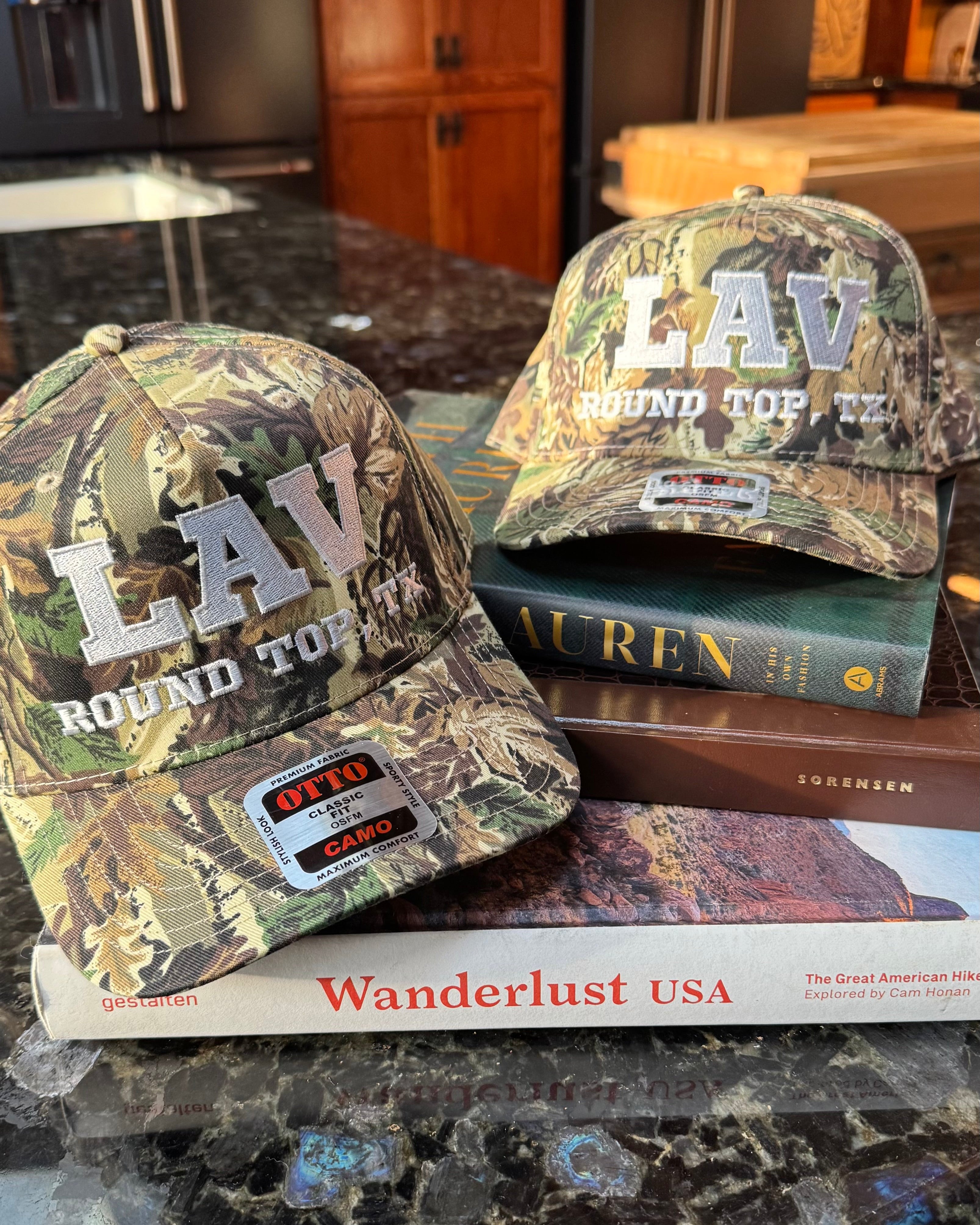 Two camouflage baseball caps with 'LAV' branding on a kitchen counter.