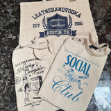 Three beige twill cotton tote bags with different limited edition designs and the 'Leatherandvodka' logo printed in blue.