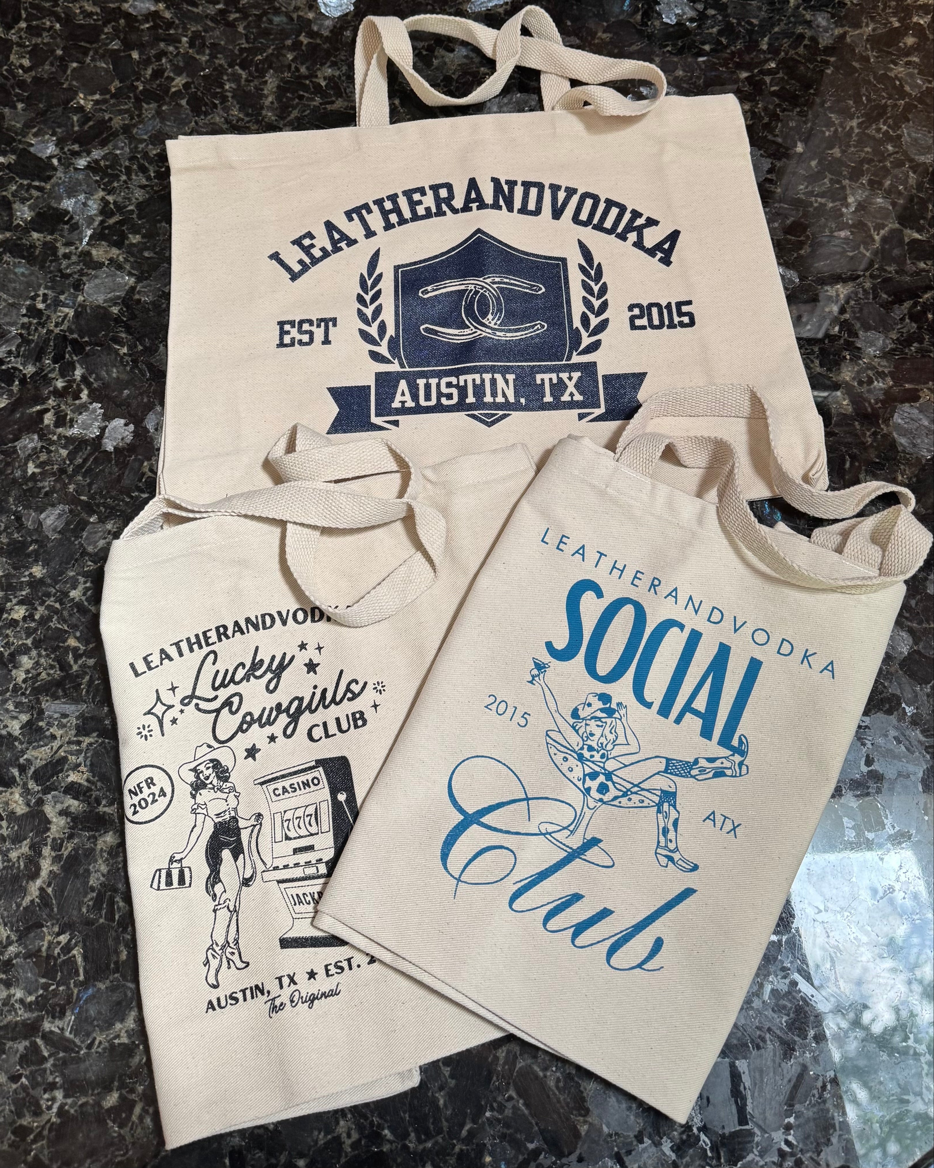 Three beige twill cotton tote bags with different limited edition designs and the 'Leatherandvodka' logo printed in blue.