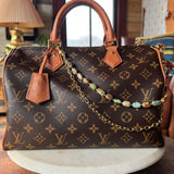 Designer handbag with monogram pattern on a wooden surface with bag charm, Leatherandvodka and JForks