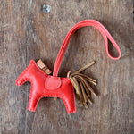 Red leather Hermes Horse keychain with tassel on a wooden surface