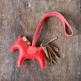 Red leather Hermes Horse keychain with tassel on a wooden surface