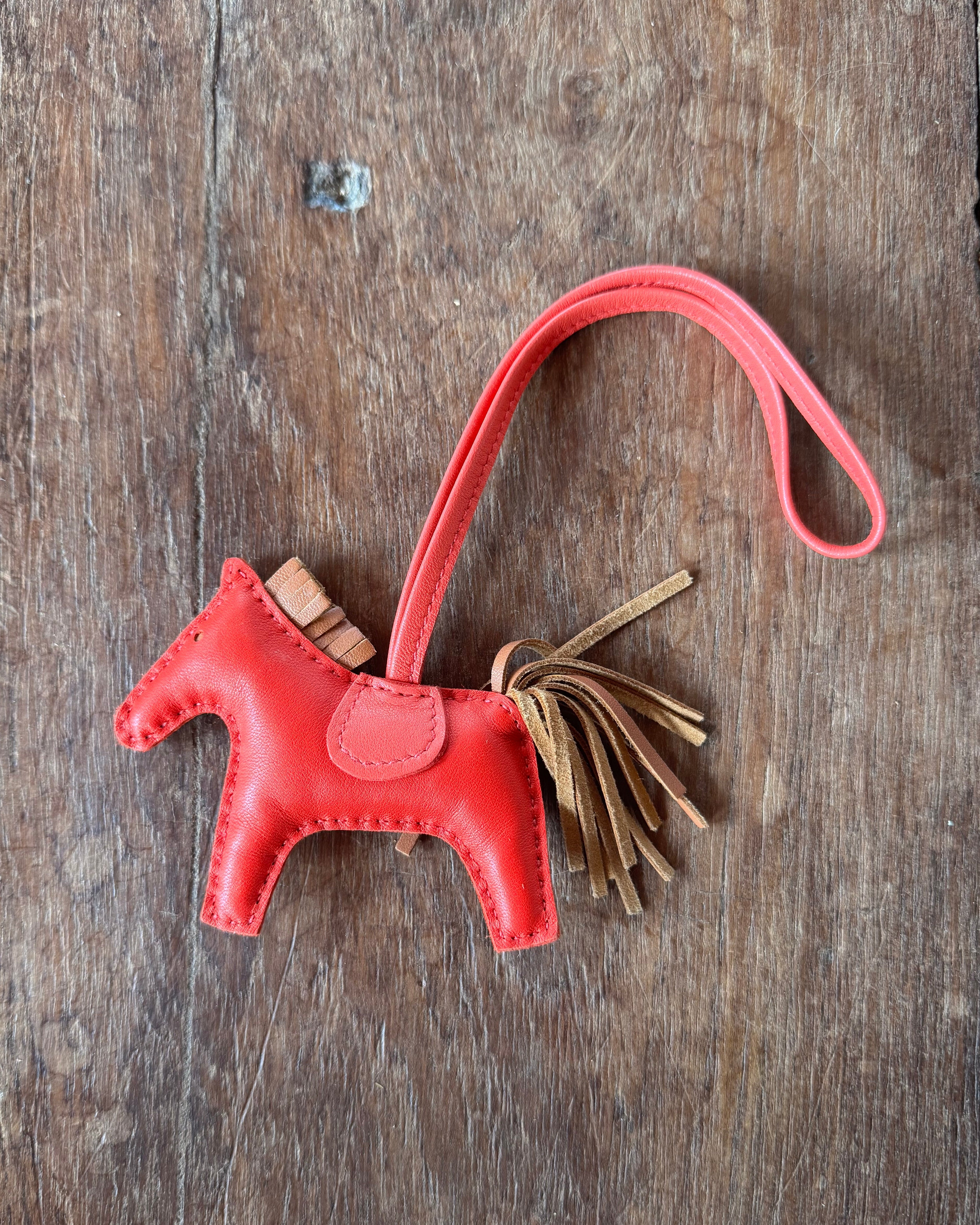 Red leather Hermes Horse keychain with tassel on a wooden surface
