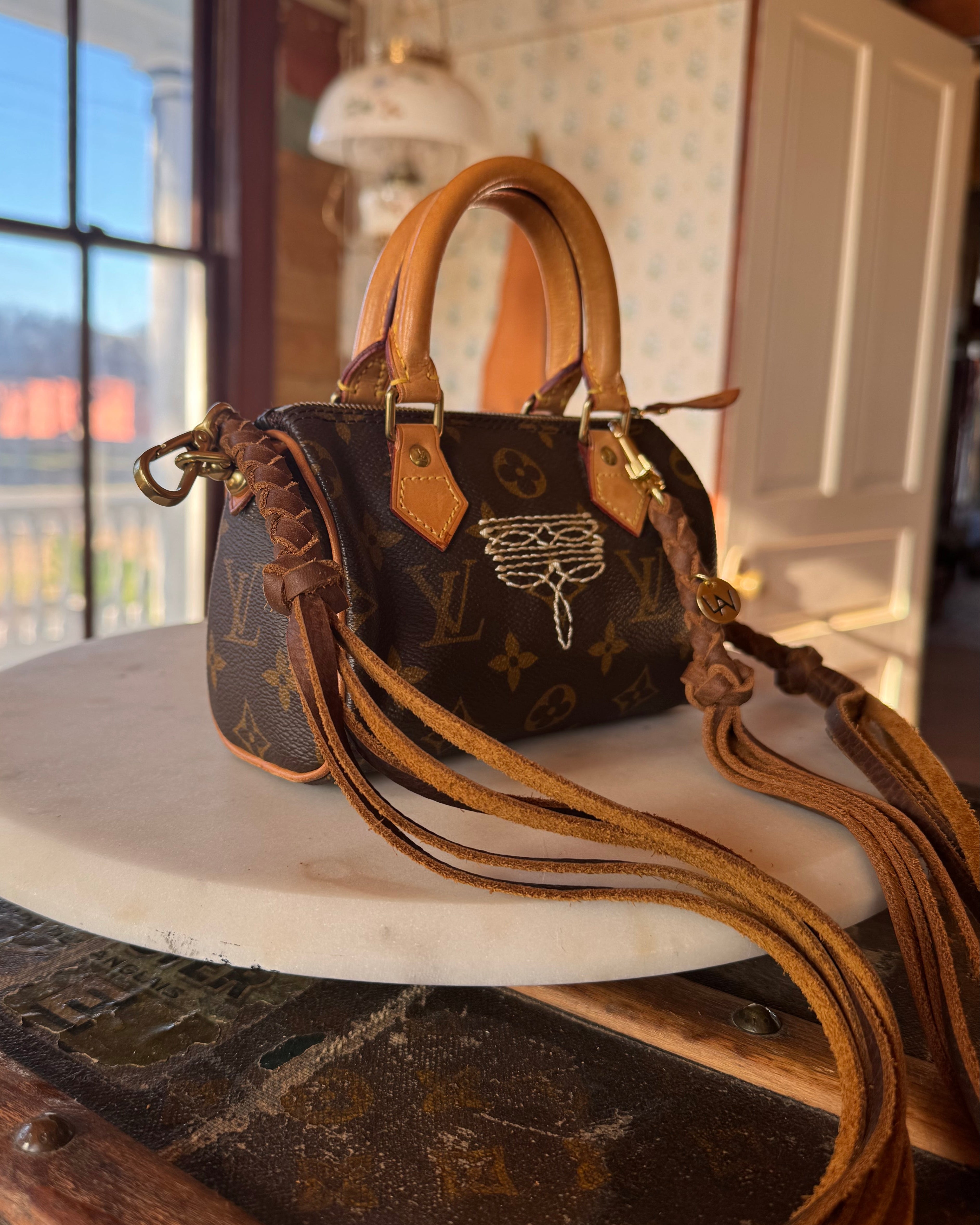 Luxury handbag with monogram pattern, revamped by Leather and Vodka with leather braided straps, sitting on wooden lift