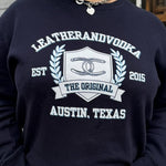 A person wearing a navy sweatshirt with 'LEATHERANDVOODKA' and 'THE ORIGINAL AUSTIN, TEXAS' printed on the front.