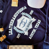 Blue crewneck with words Leatherandvodka laying on marble countertop