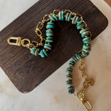 Turquoise beaded bag chain with gold chain on a wooden block, J Forks & Leather and Vodka
