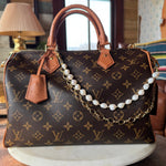 Designer handbag with monogram pattern and pearl chain on a wooden surface.