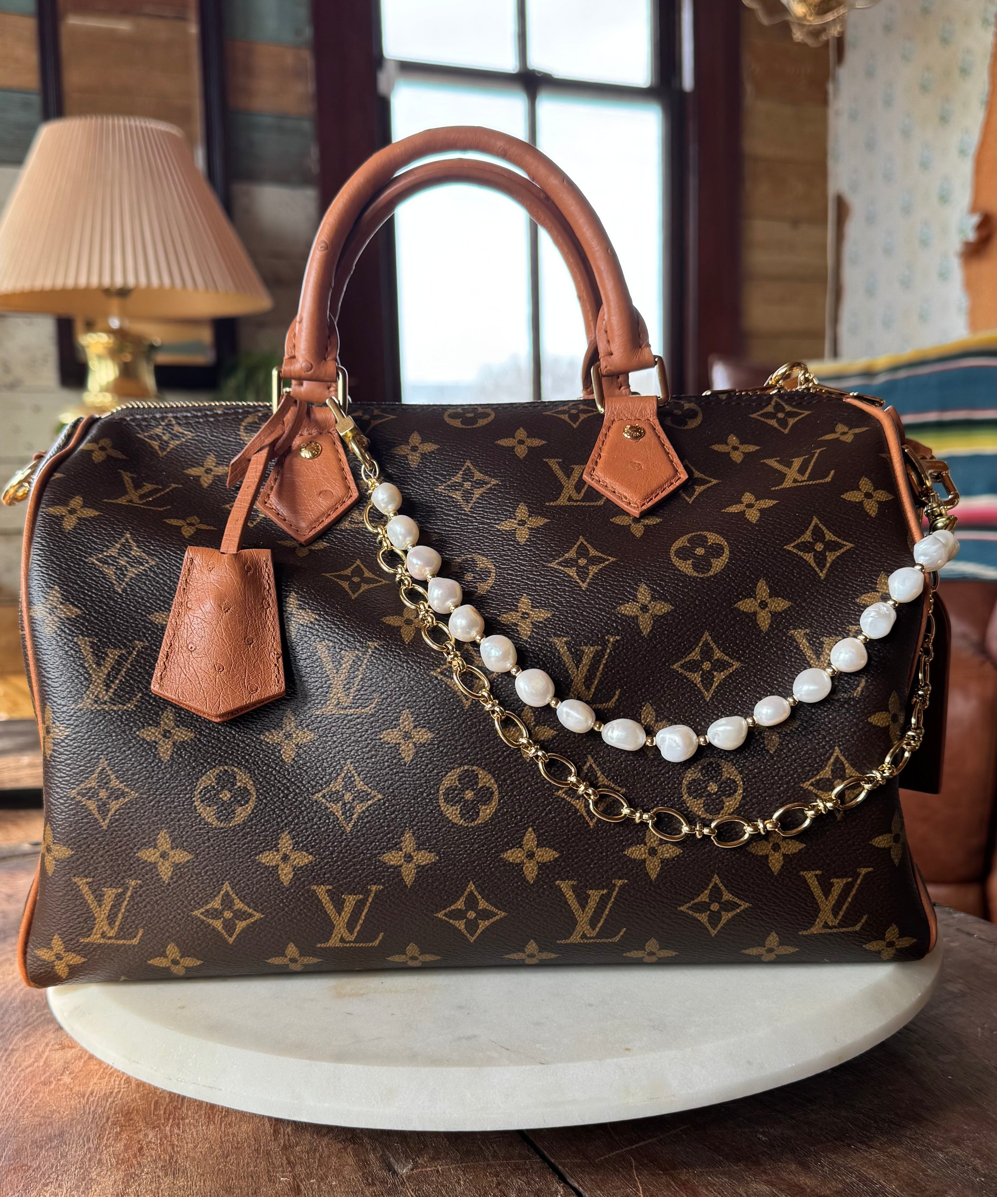 Designer handbag with monogram pattern and pearl chain on a wooden surface.