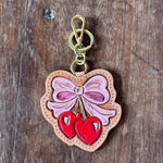 Decorative keychain with a pink bow and red hearts on a wooden surface