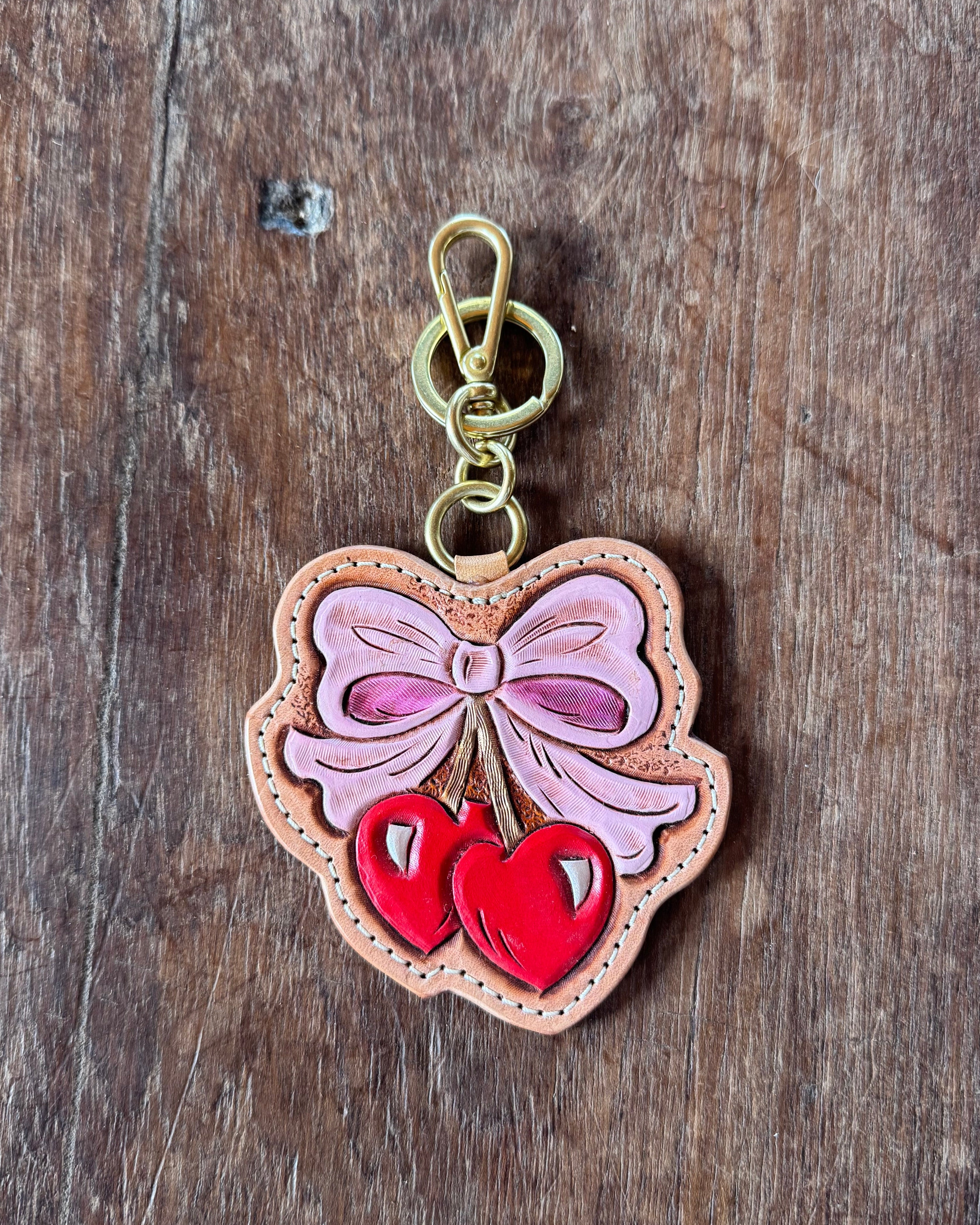 Decorative keychain with a pink bow and red hearts on a wooden surface