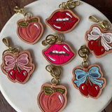 Colorful lip, bow, and fruit-shaped keychains on a marble plate.