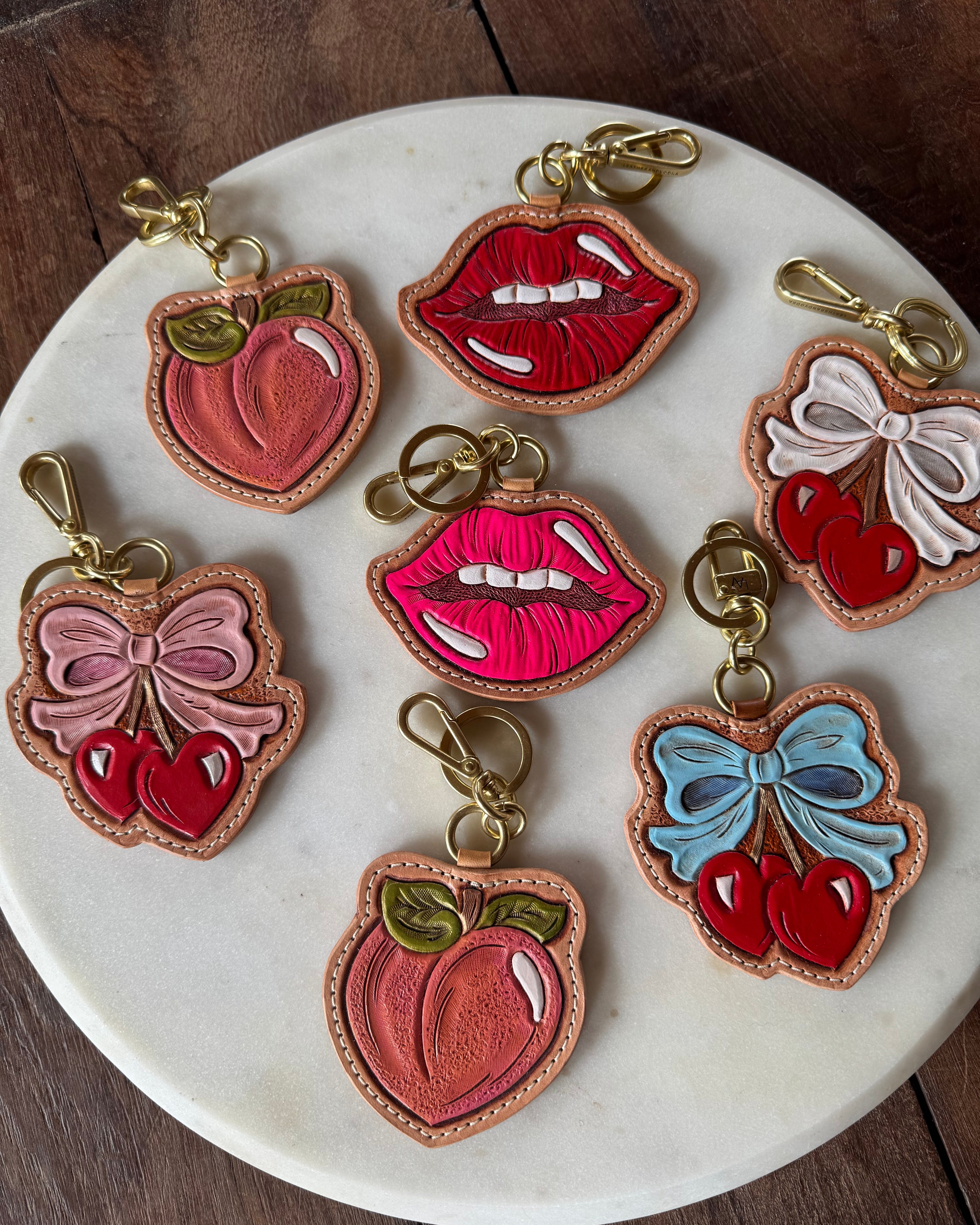 Colorful lip, bow, and fruit-shaped keychains on a marble plate.