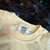 Beige t-shirt with a 'Comfort Colors' tag against a dark textured background