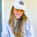 Woman wearing a white cap with a logo, standing in front of a building with a blue door.