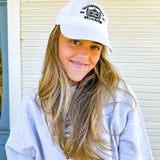 Woman wearing a white cap with a logo, standing in front of a building with a blue door.