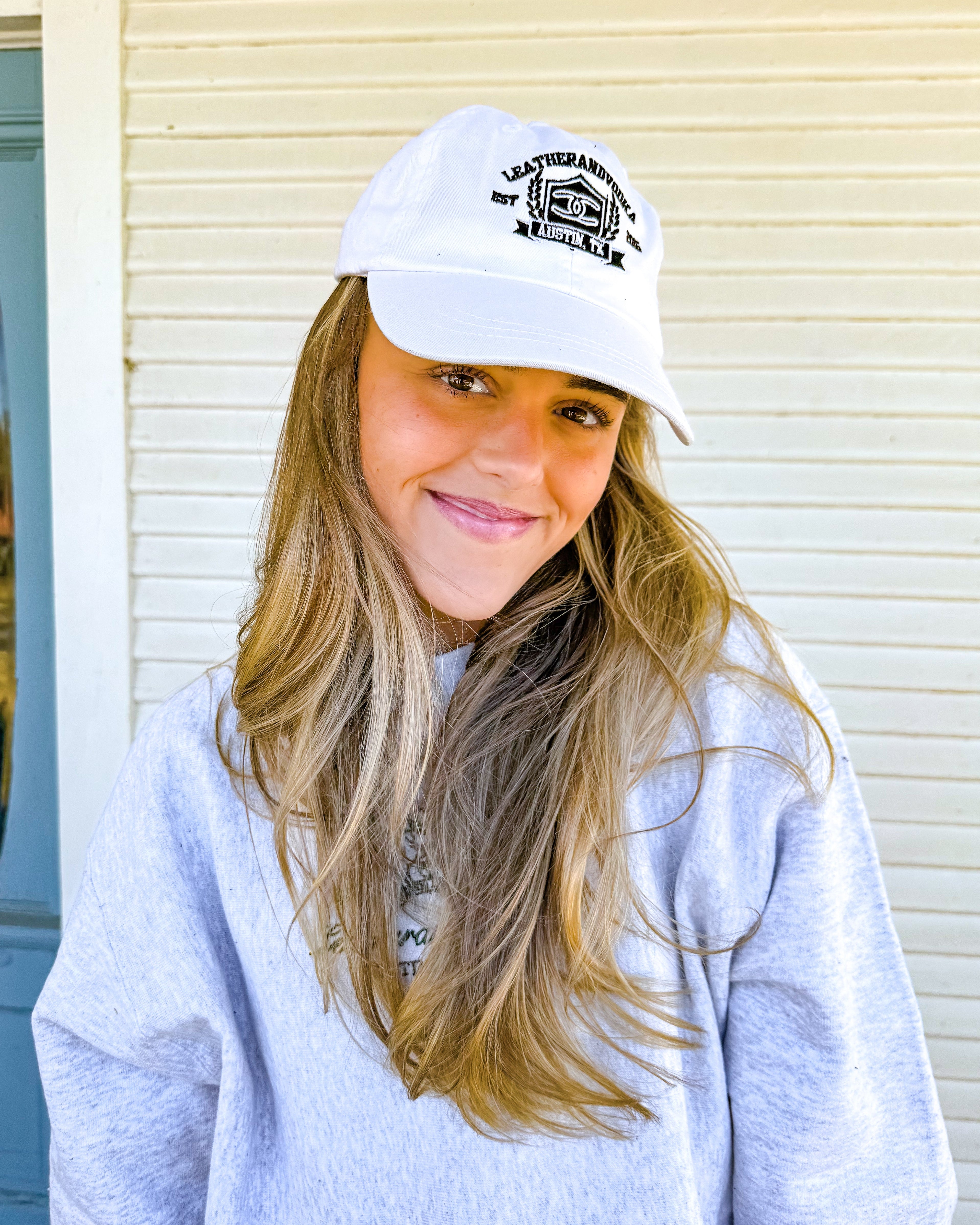 Woman wearing a white cap with a logo, standing in front of a building with a blue door.