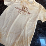 White t-shirt with brown logo and text on a dark surface