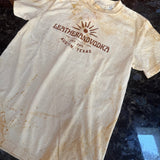 White t-shirt with brown logo and text on a dark surface