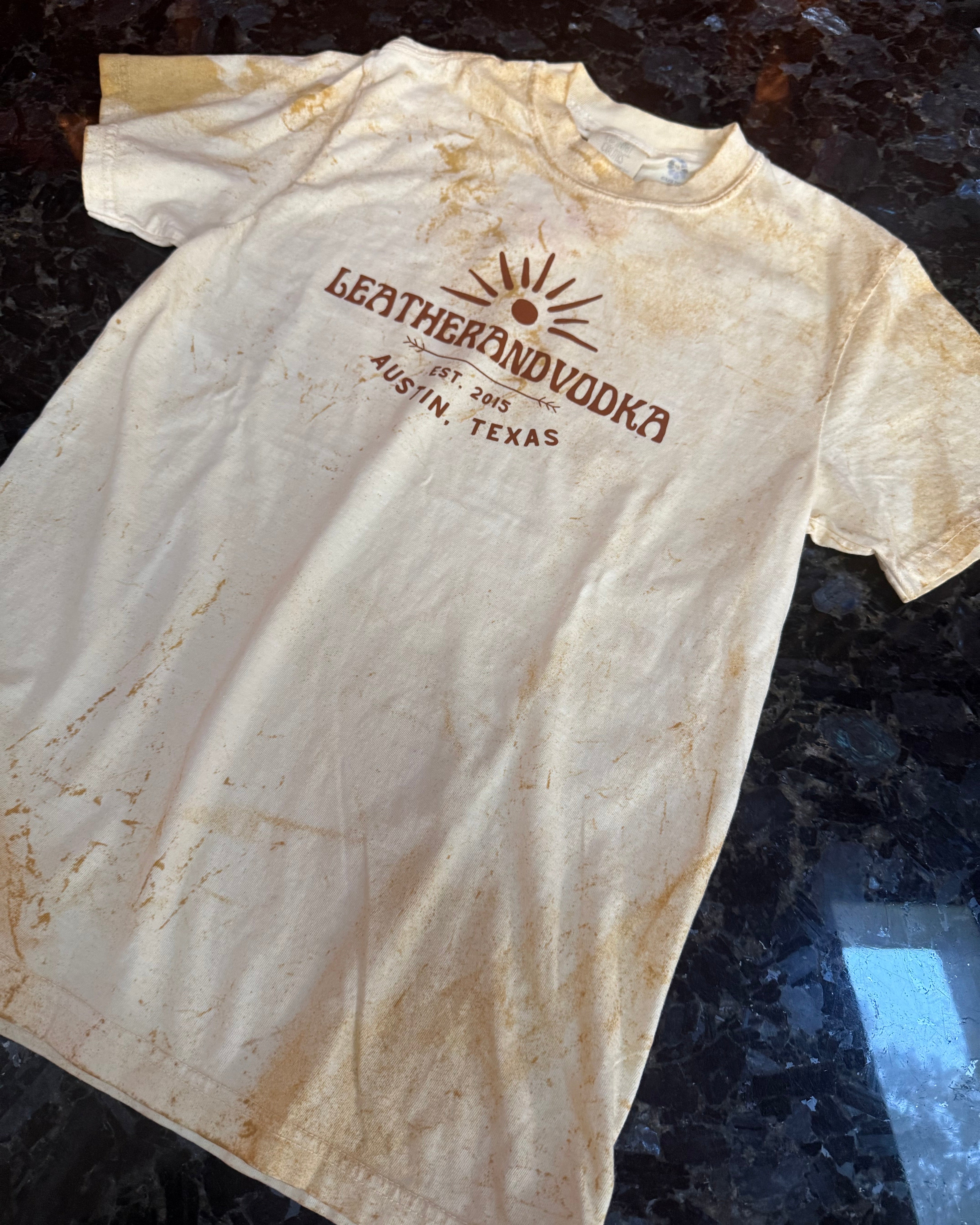 White t-shirt with brown logo and text on a dark surface