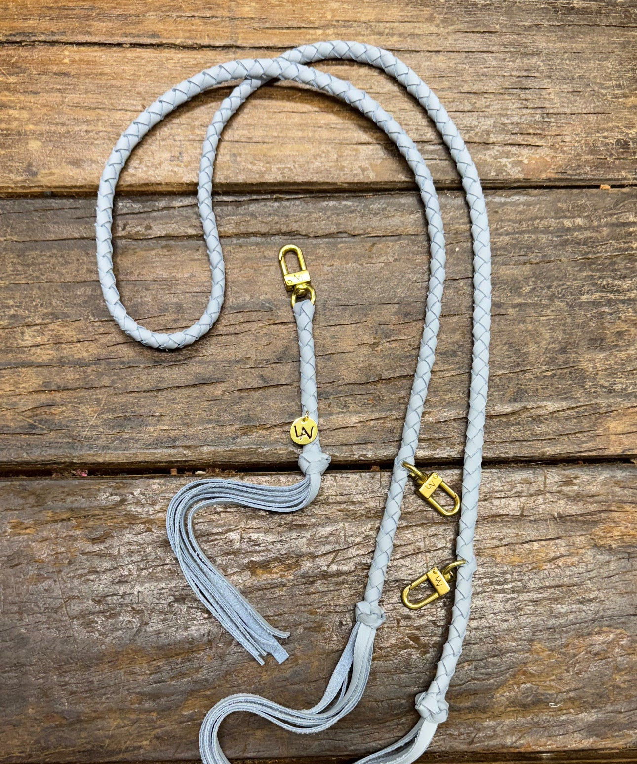 Powder blue leather bag strap with gold clasps on a wooden surface