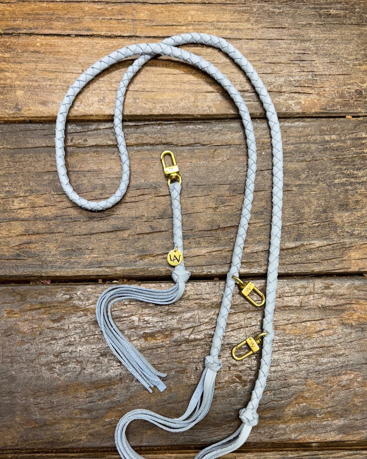 Powder blue leather bag strap with gold clasps on a wooden surface