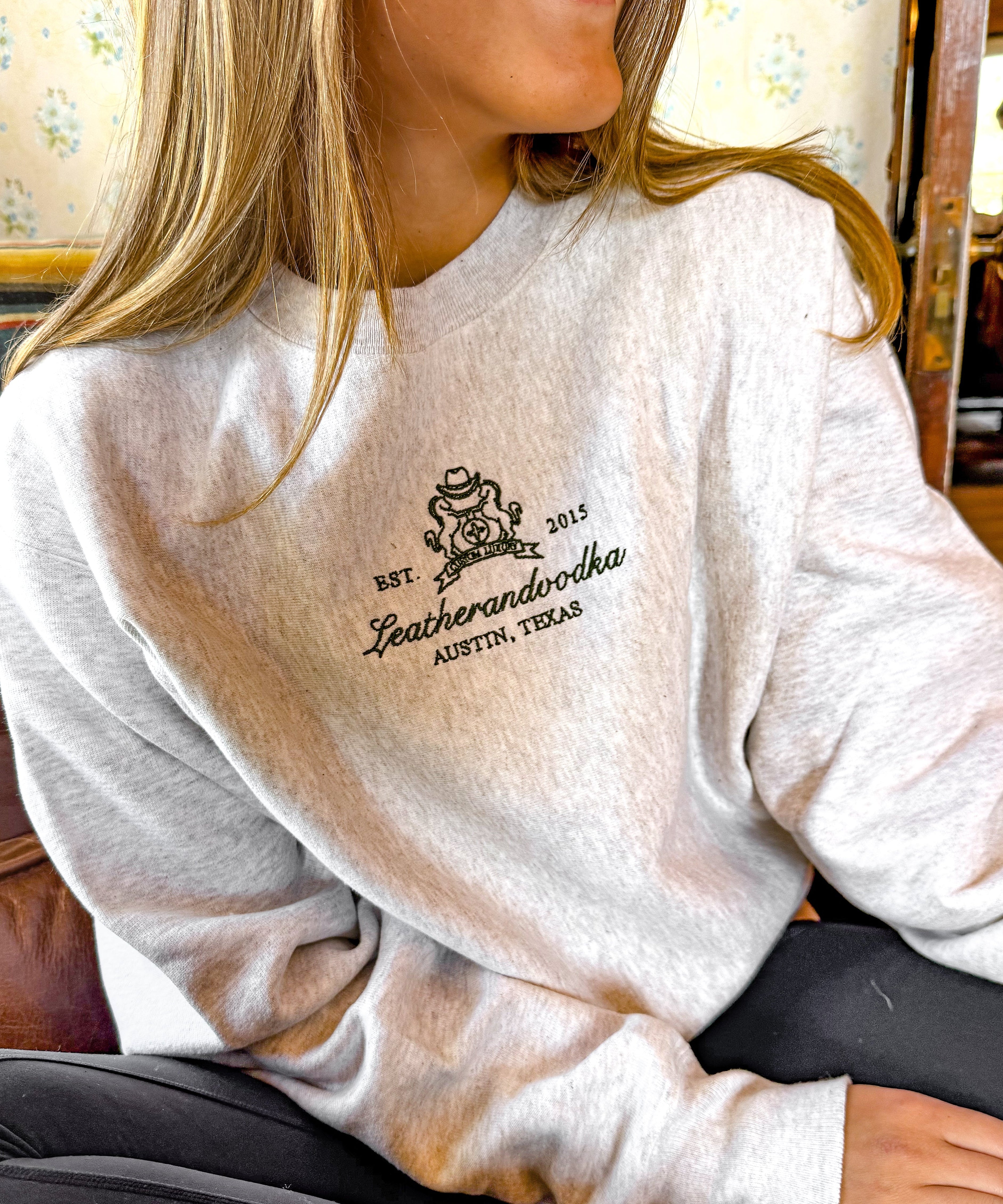 Person wearing a white sweatshirt with a logo and text, sitting indoors.